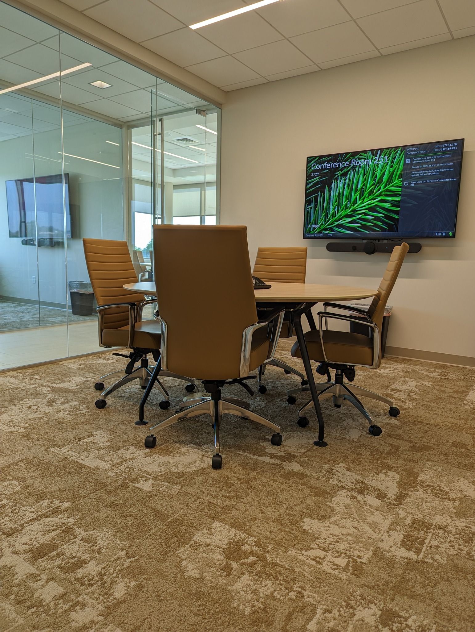 Conference room with a table, chairs, TV, and glass wall. Carpeted floor with a neutral pattern.