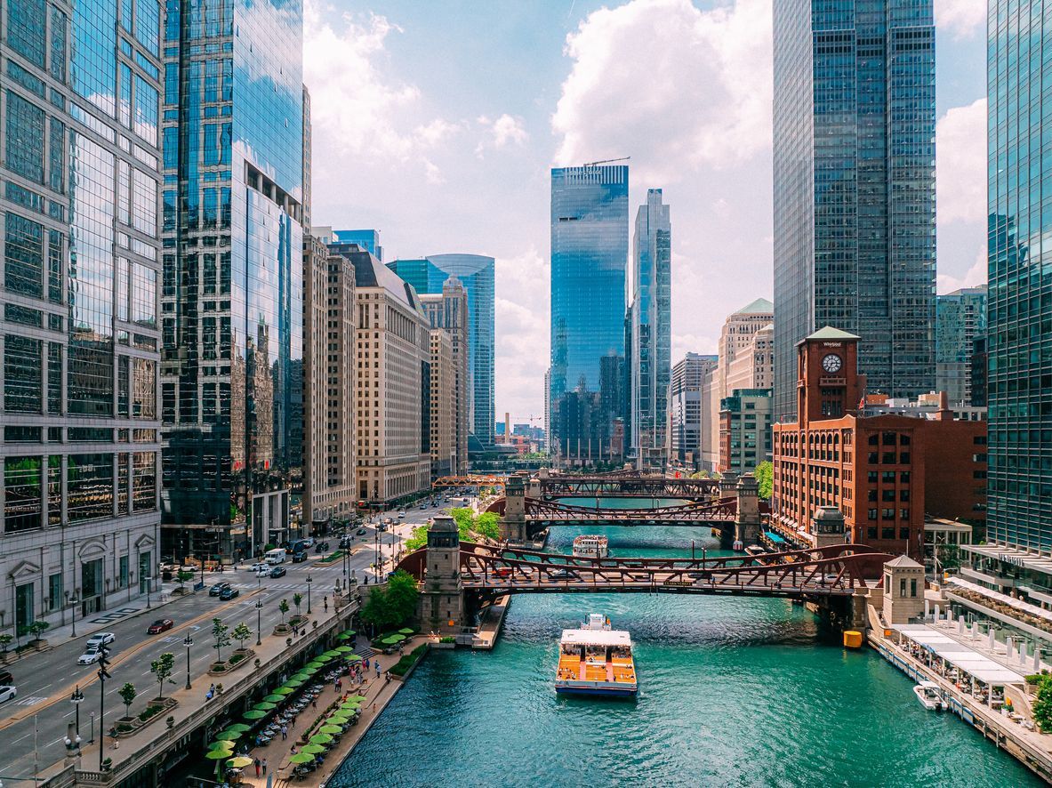Chicago River with boats and bridges, surrounded by tall buildings on a sunny day.