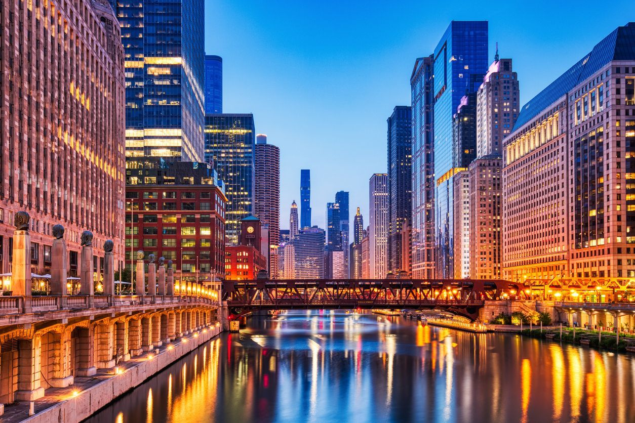 Chicago River at dusk, reflecting city lights and buildings; a bridge crosses the water.