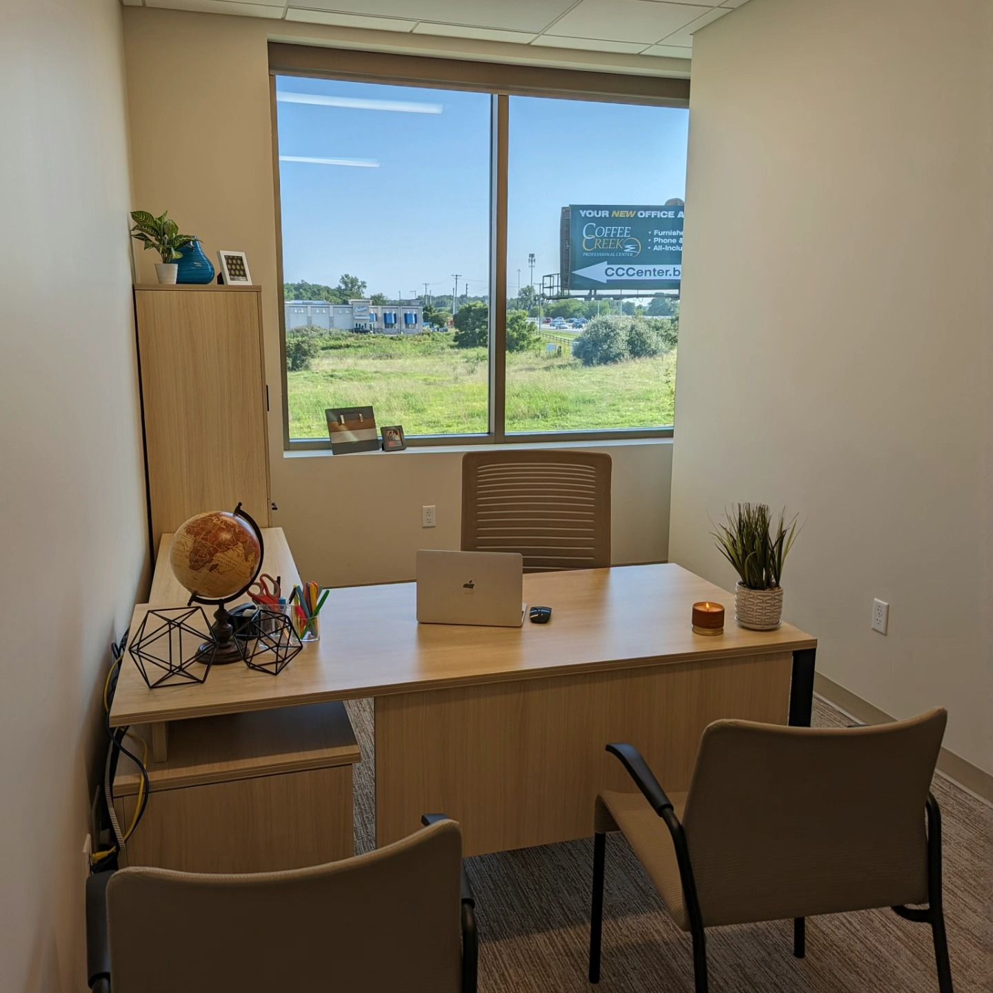 Office with desk, chairs, and window overlooking a grassy field. A laptop sits on the desk.