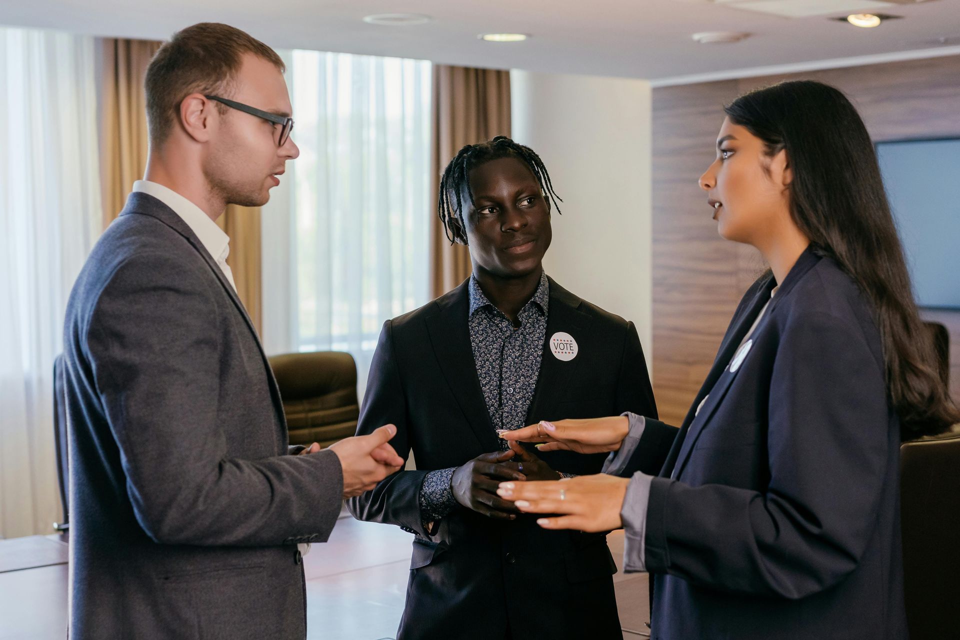 Three people in suits discussing in a modern meeting room.