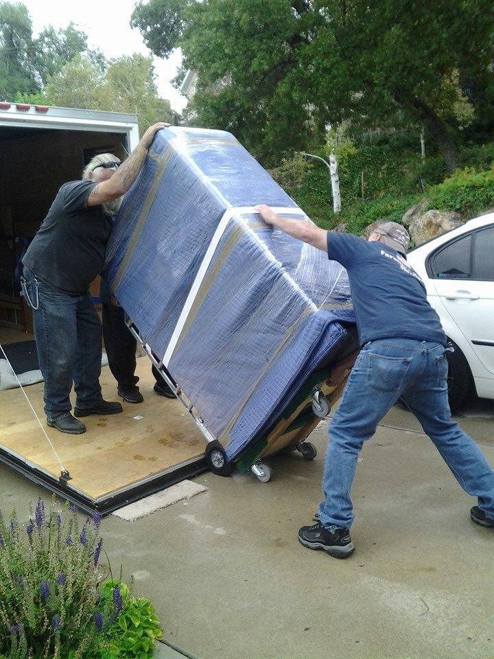 A man is pushing a mattress on a dolly into a truck.