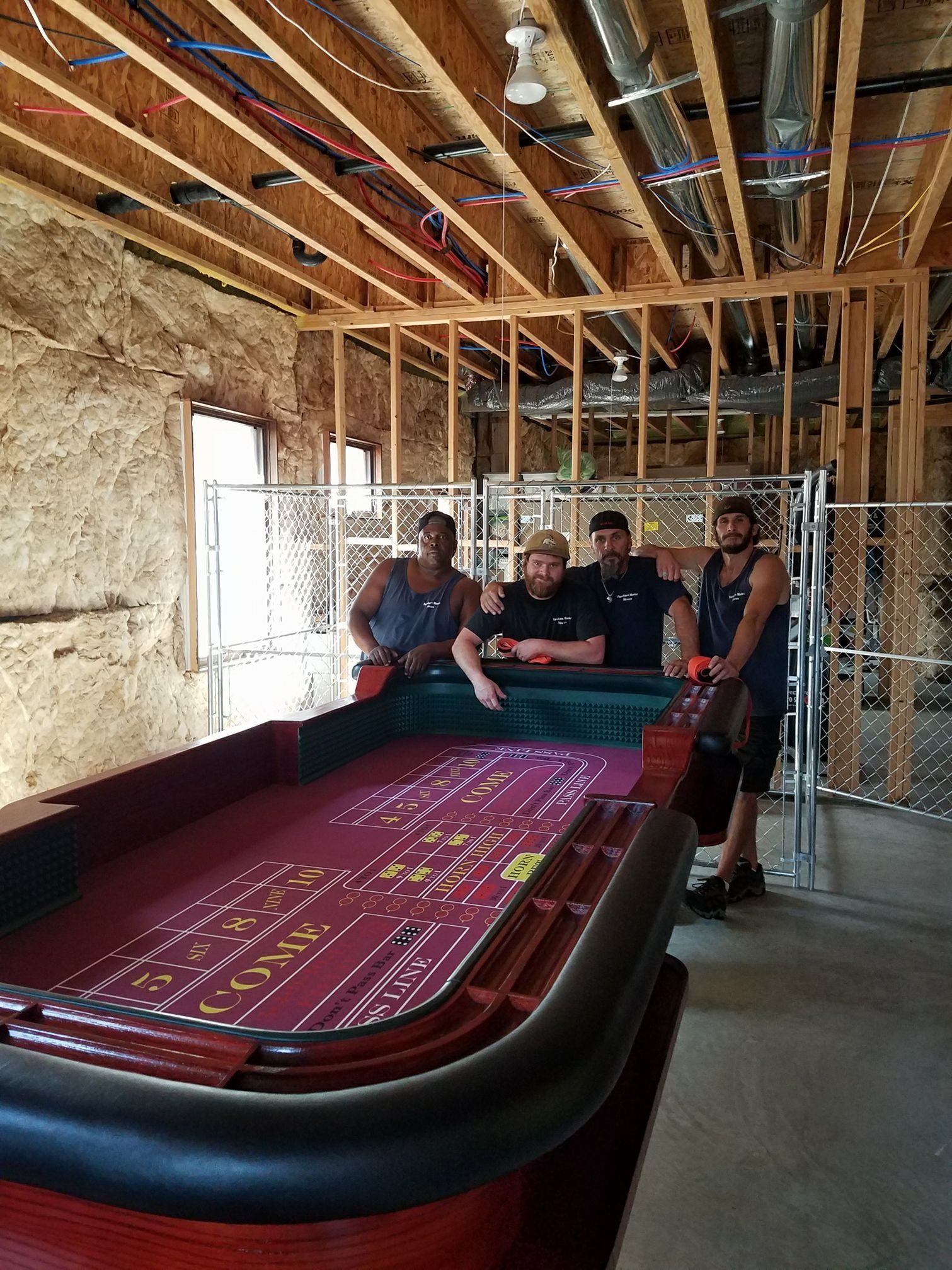 A group of men are standing around a roulette table in a room under construction.