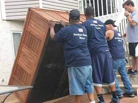 A group of men in blue shirts are carrying a large wooden box