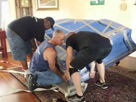 Three men are moving a piano in a living room.