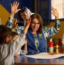 A woman is sitting at a table with a group of children.