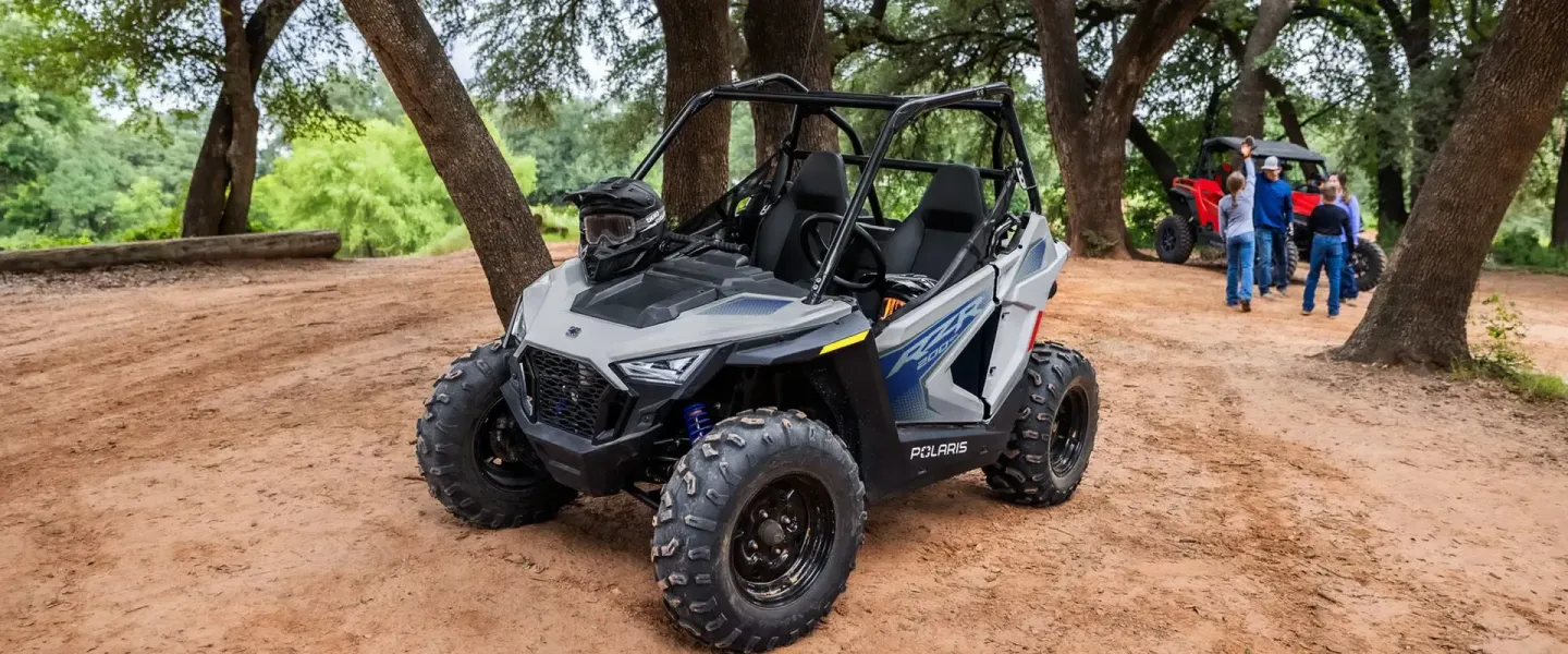 A white atv is parked on a dirt road next to trees.