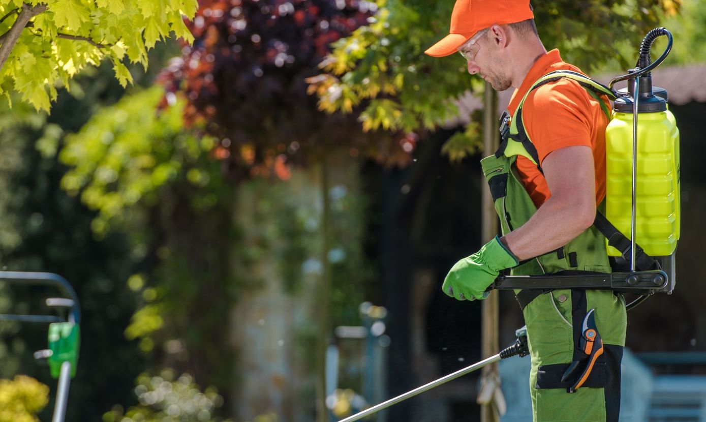 Man in orange and green protective gear spraying chemicals outdoors.