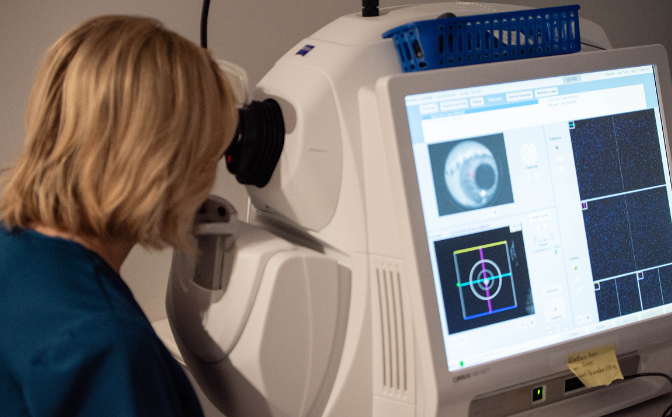 A woman in a blue scrub is looking at a computer screen.