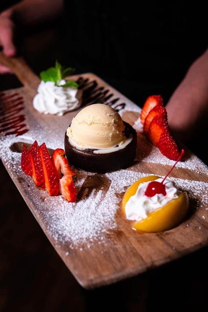 A wooden cutting board topped with desserts and fruit.