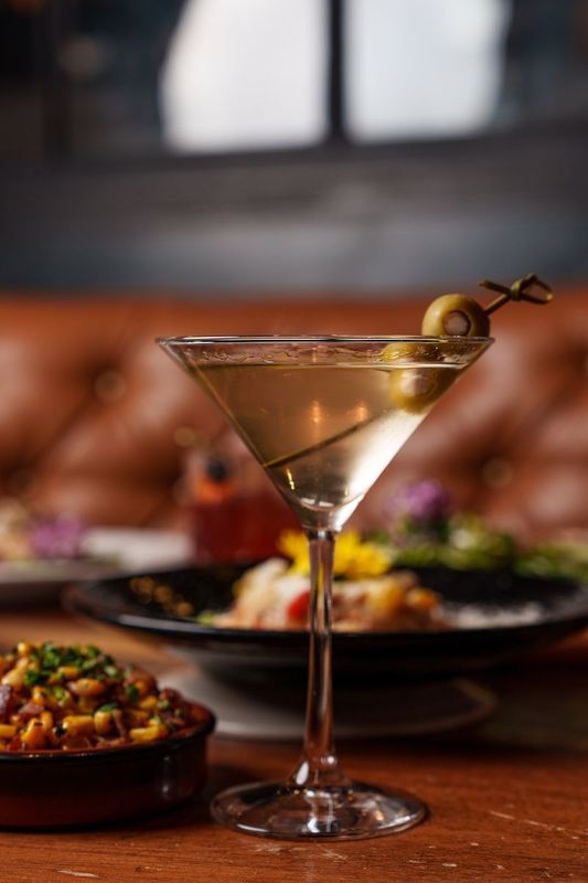 A martini with an olive on a stick is on a table.