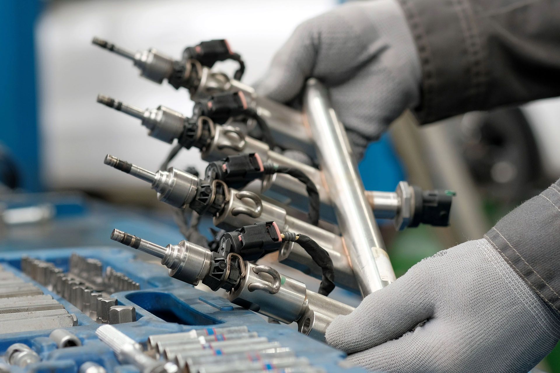 Mechanic holding a fuel injector rail with multiple injectors. Tools are in a blue tray.
