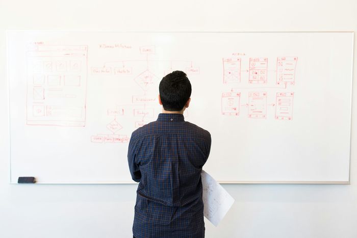 Un homme se tient devant un tableau blanc et regarde un diagramme.