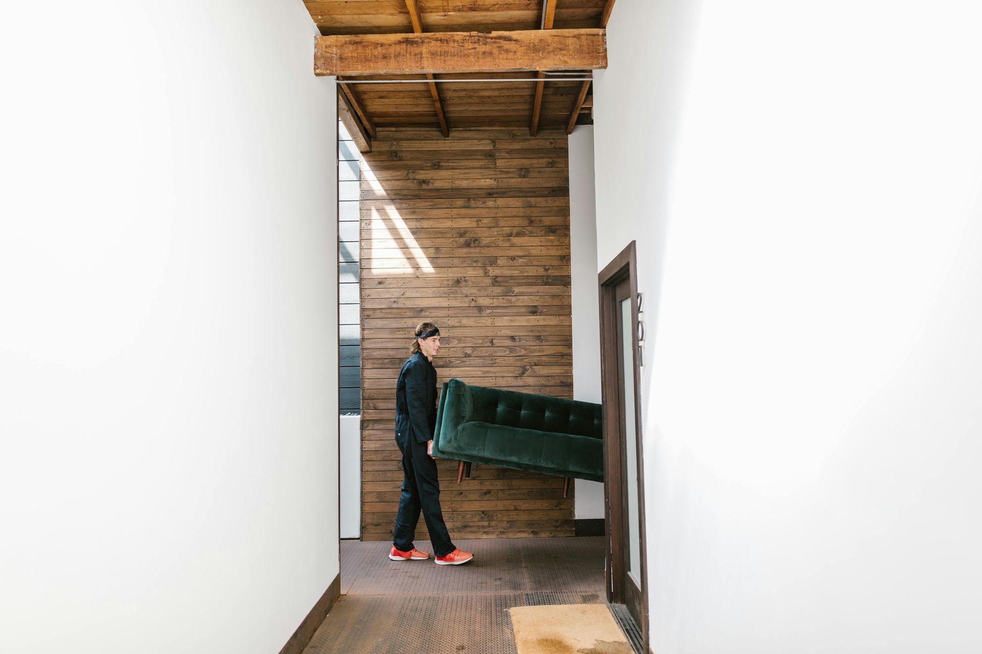 Un homme porte un canapé vert dans un couloir.