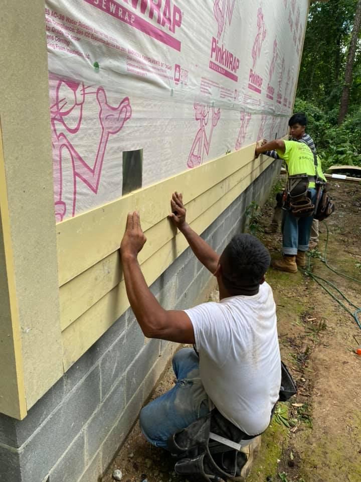 A man is installing siding on the side of a building.