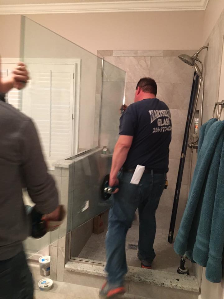 A man is installing a glass shower door in a bathroom.