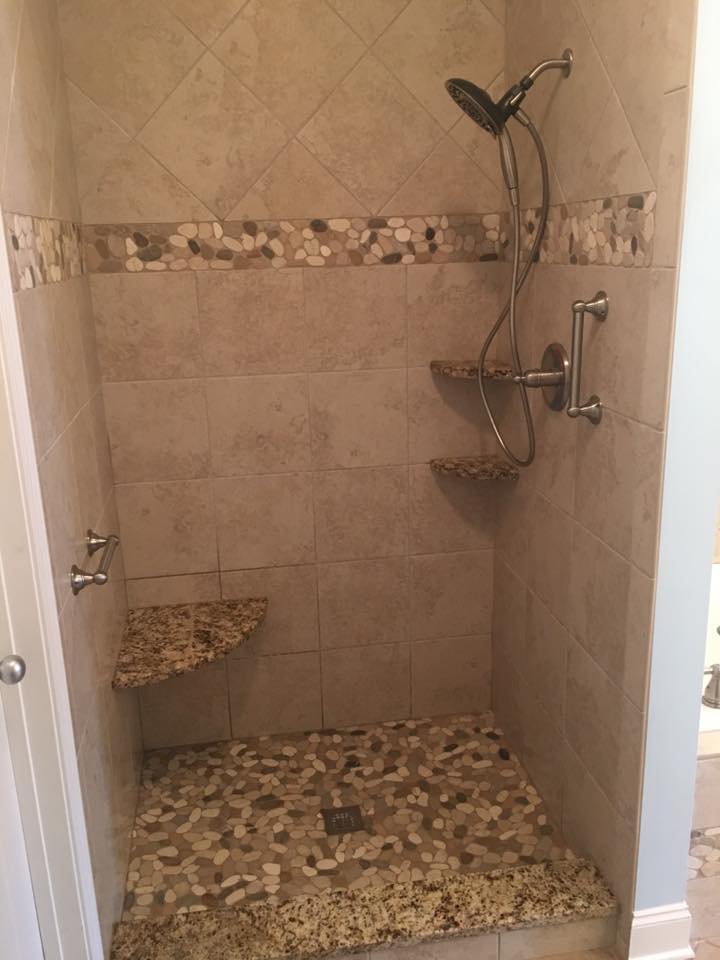 A walk in shower with a bench and a shower head.