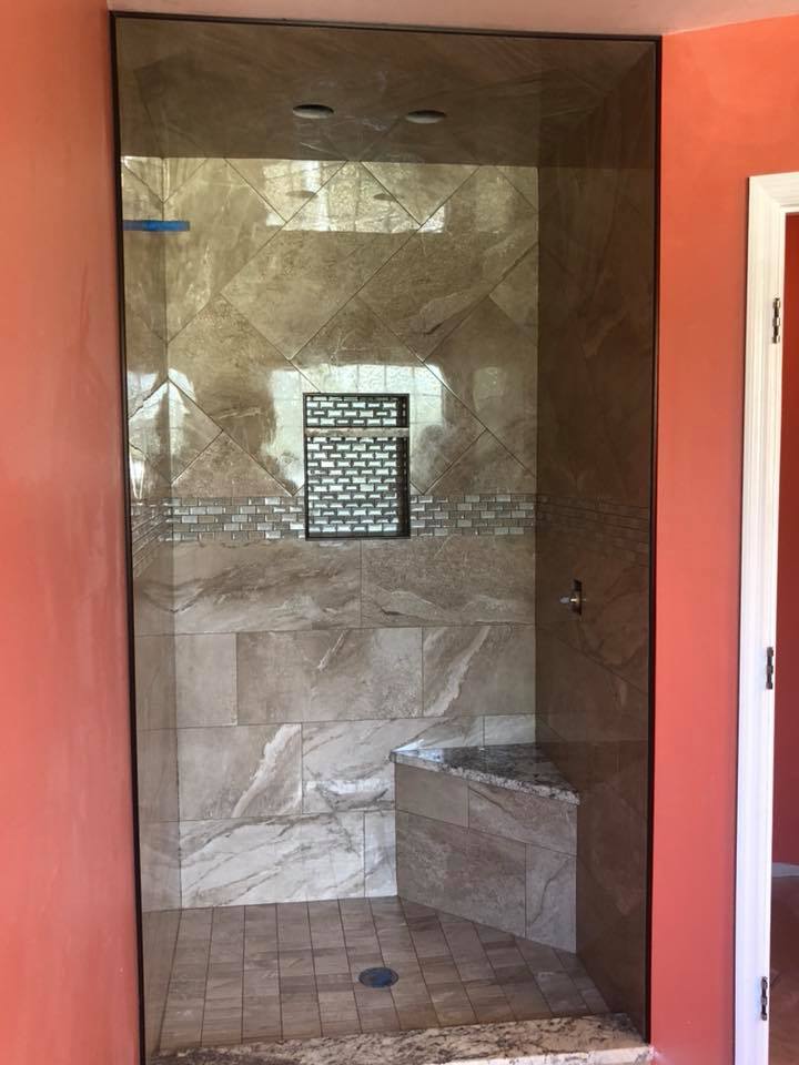 A shower with a glass door and a bench in a bathroom.
