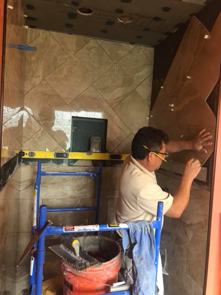 A man is standing on a ladder working on a tile wall.