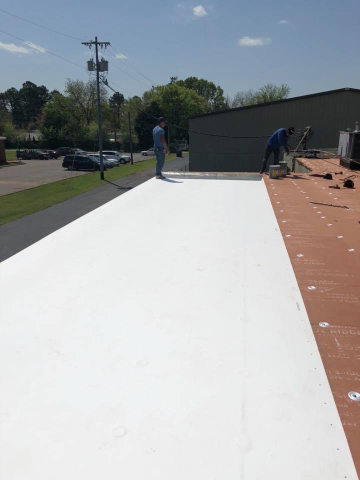 A man is standing on top of a white roof.