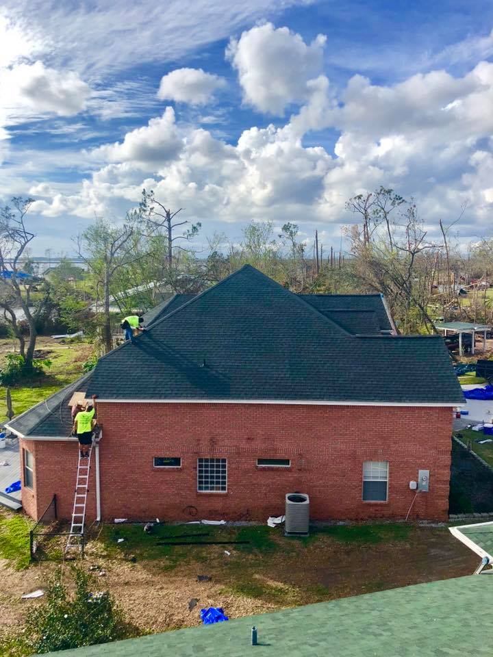 Two men are working on the roof of a brick house.