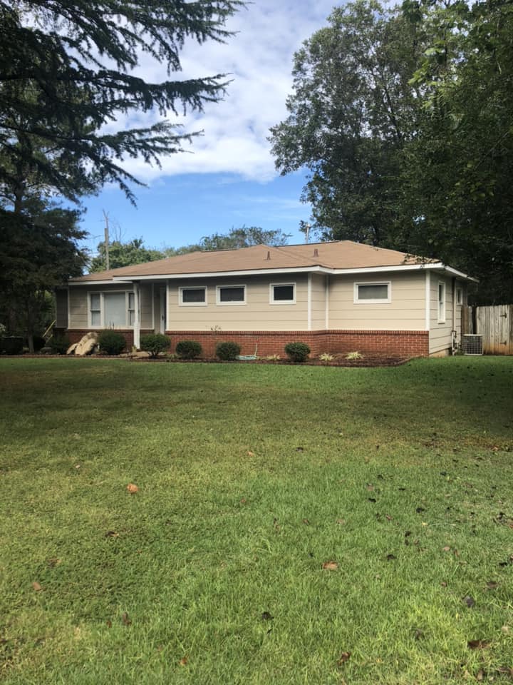 A house with a large lawn in front of it and trees in the background.