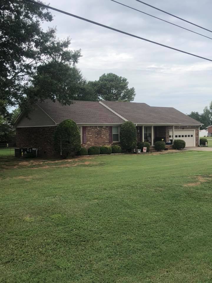 A brick house with a brown roof is sitting on top of a lush green field.