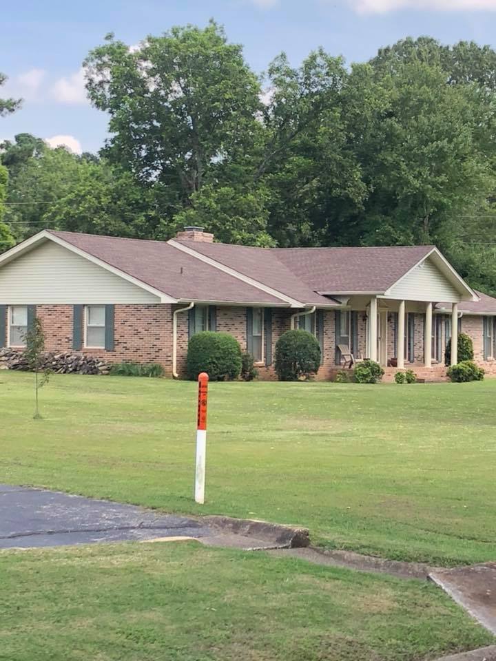 A brick house with a brown roof and a large lawn in front of it.