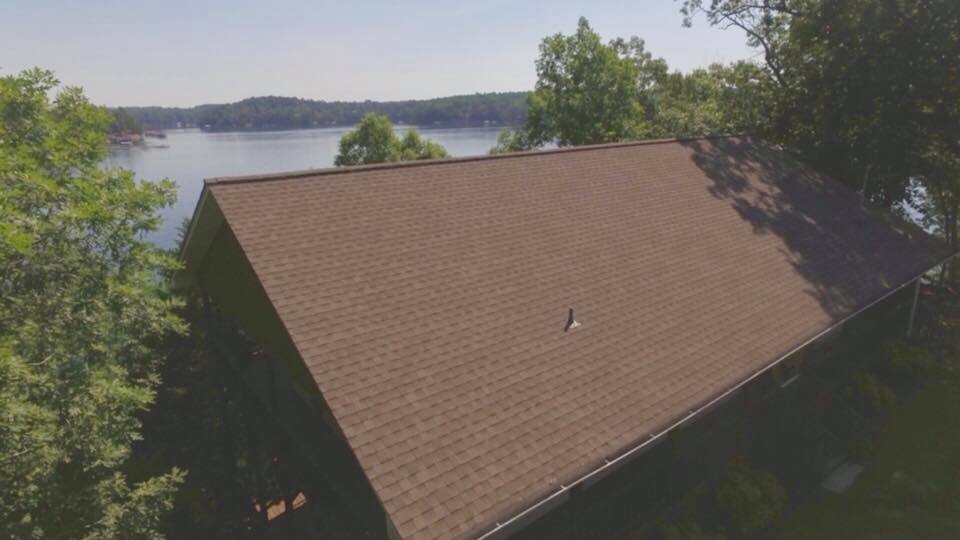 An aerial view of a house with a roof overlooking a lake.