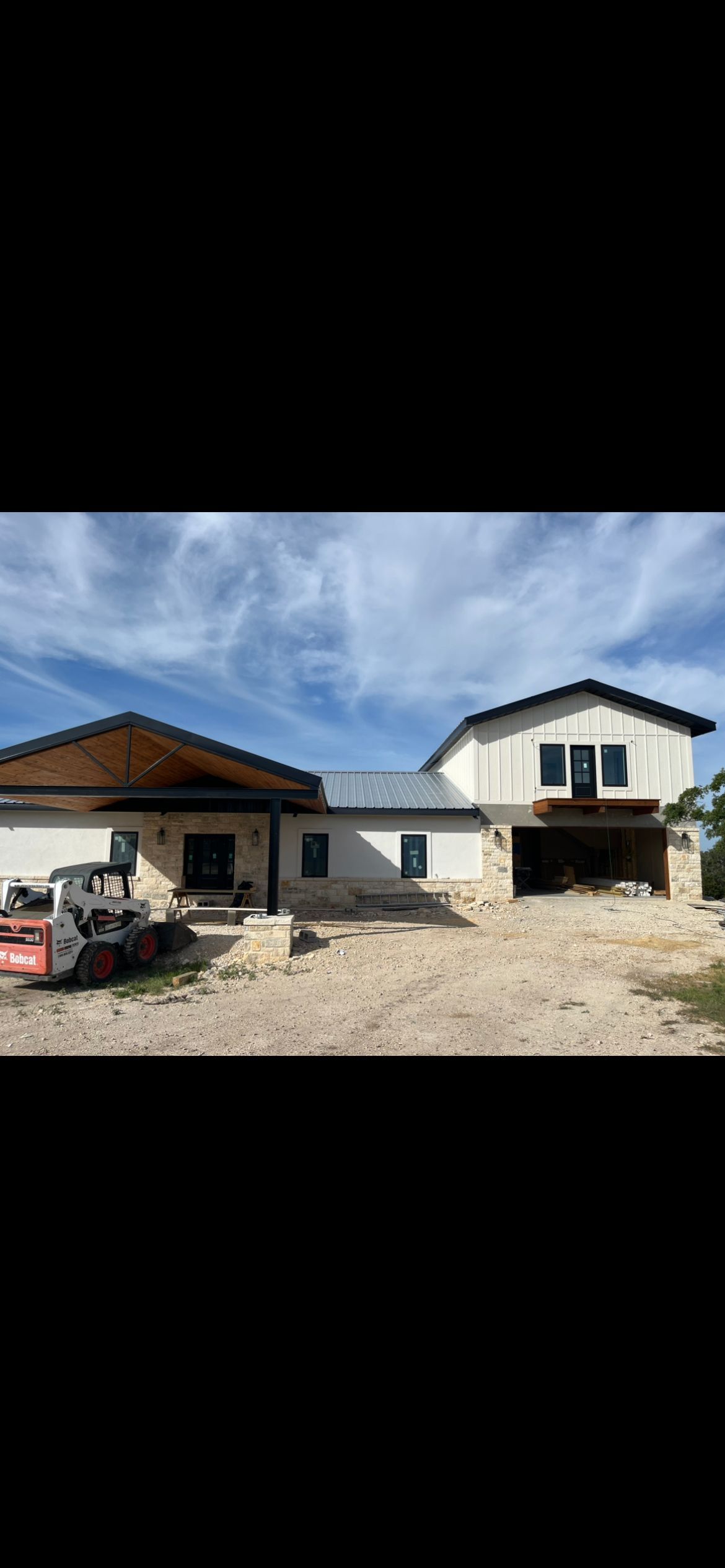 Exterior of a light-colored building under construction, cloudy blue sky overhead. A small red construction vehicle is parked.