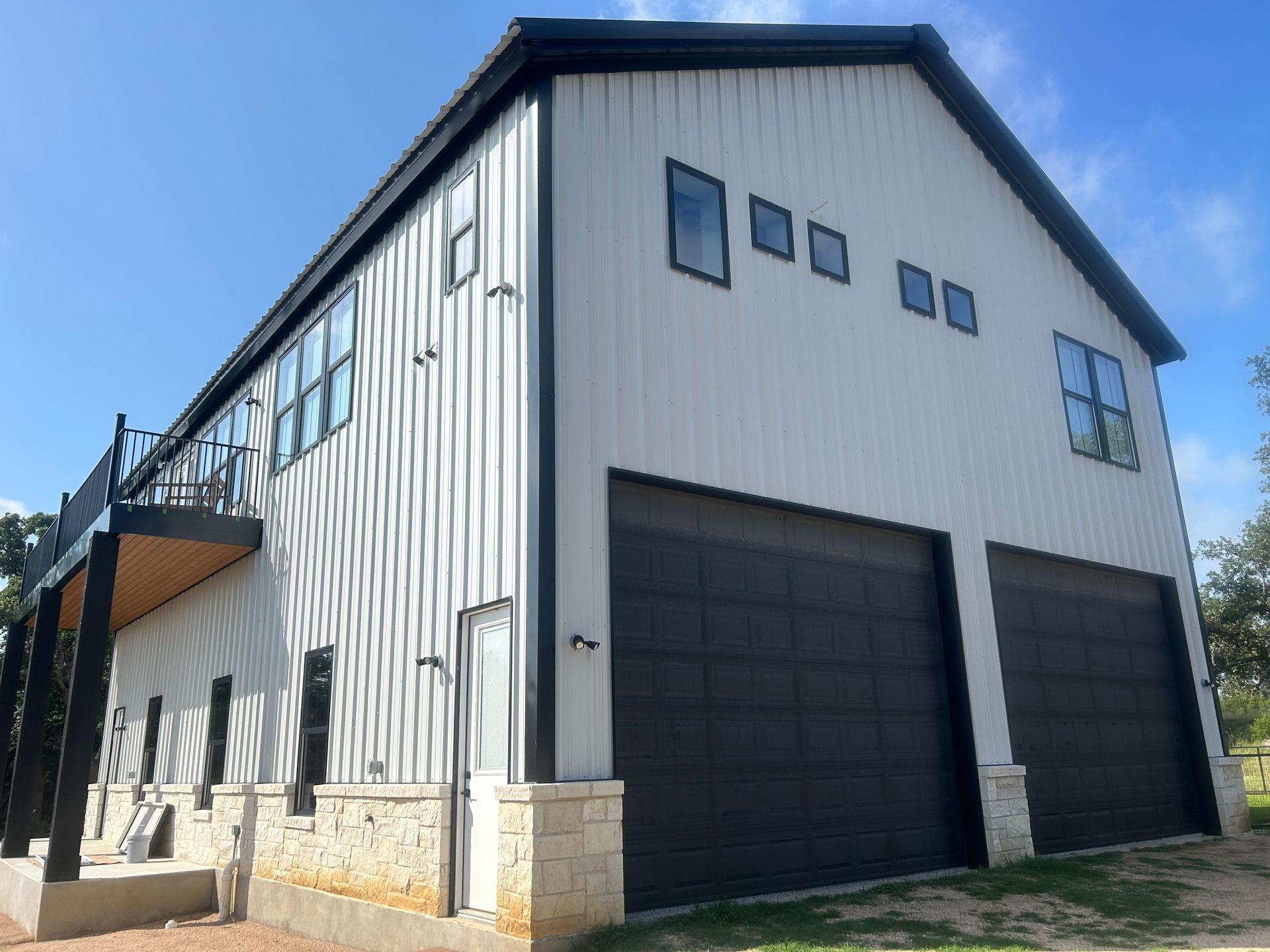 White and black metal barn-style building with two garage doors, windows, and a balcony.