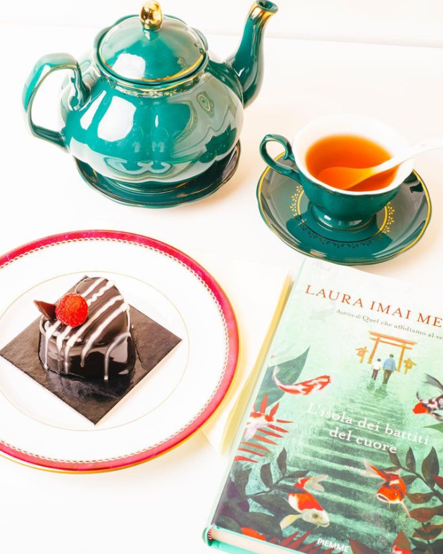 una teiera , una tazza di tè , un piatto di torta e un libro di laura imai me