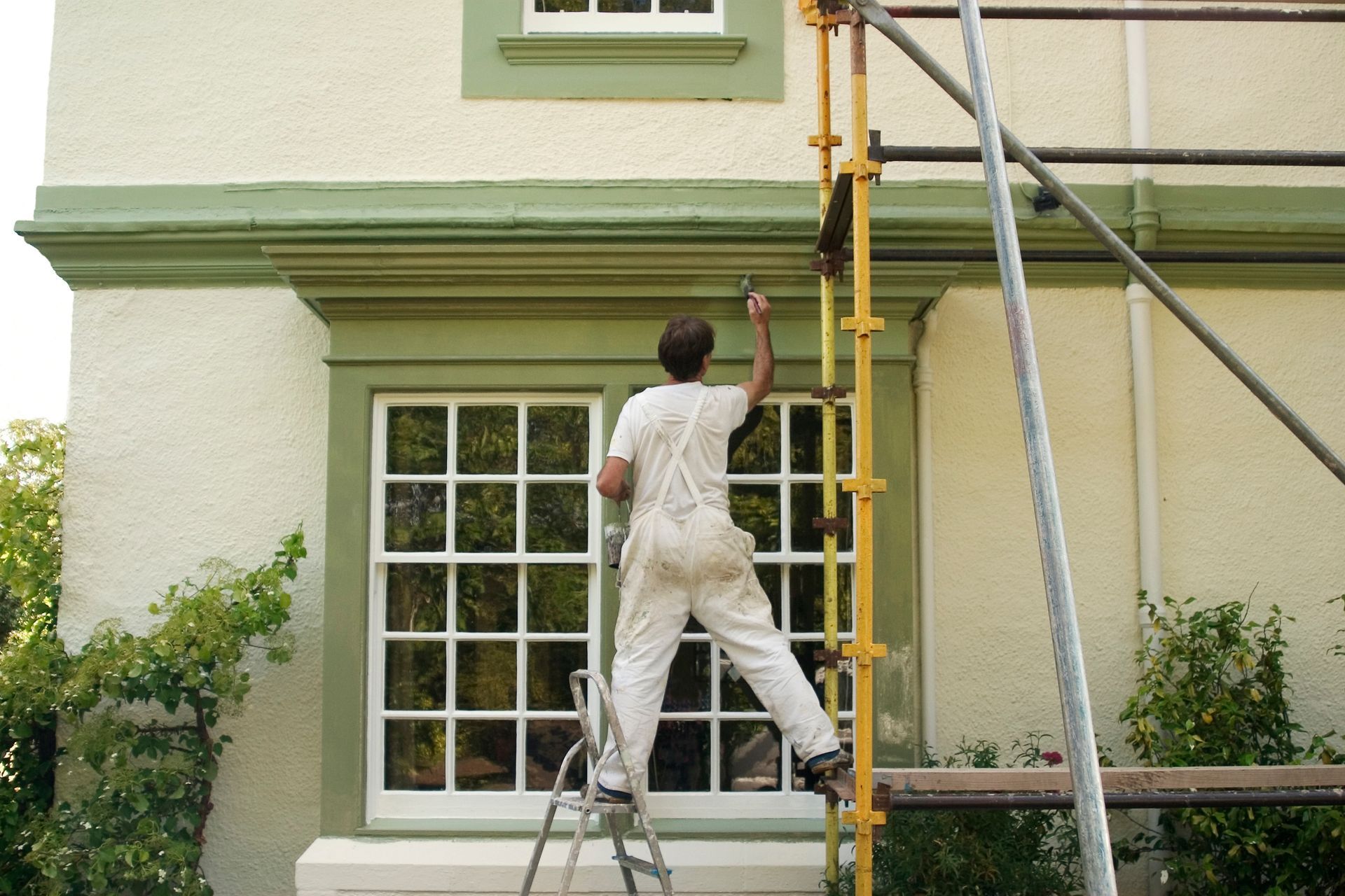 Exterior house painting in progress, with a painter applying fresh paint to a home's trim and fascia