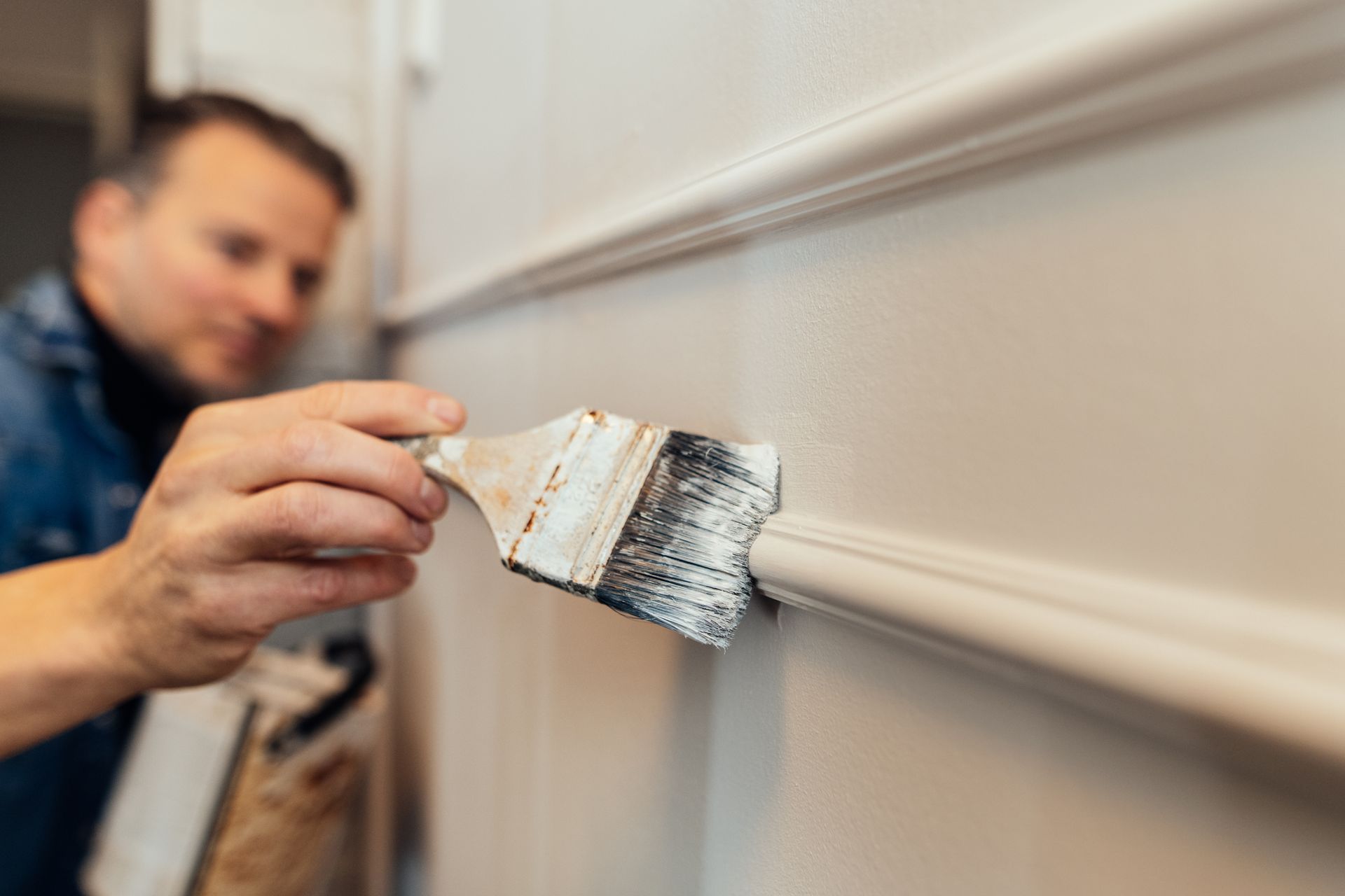 A man painting a modern wall with wainscot panel.