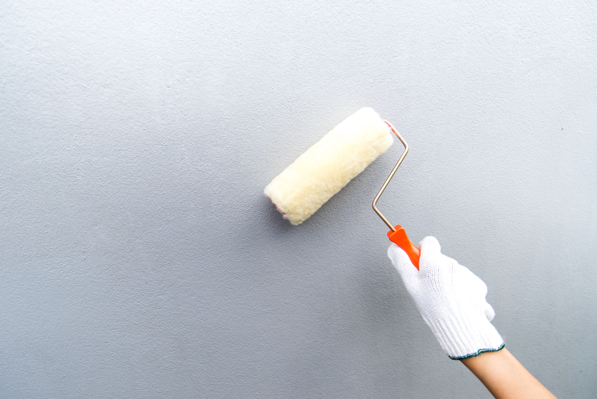 Gloved hand holds a point roller against a wall with gray paint.