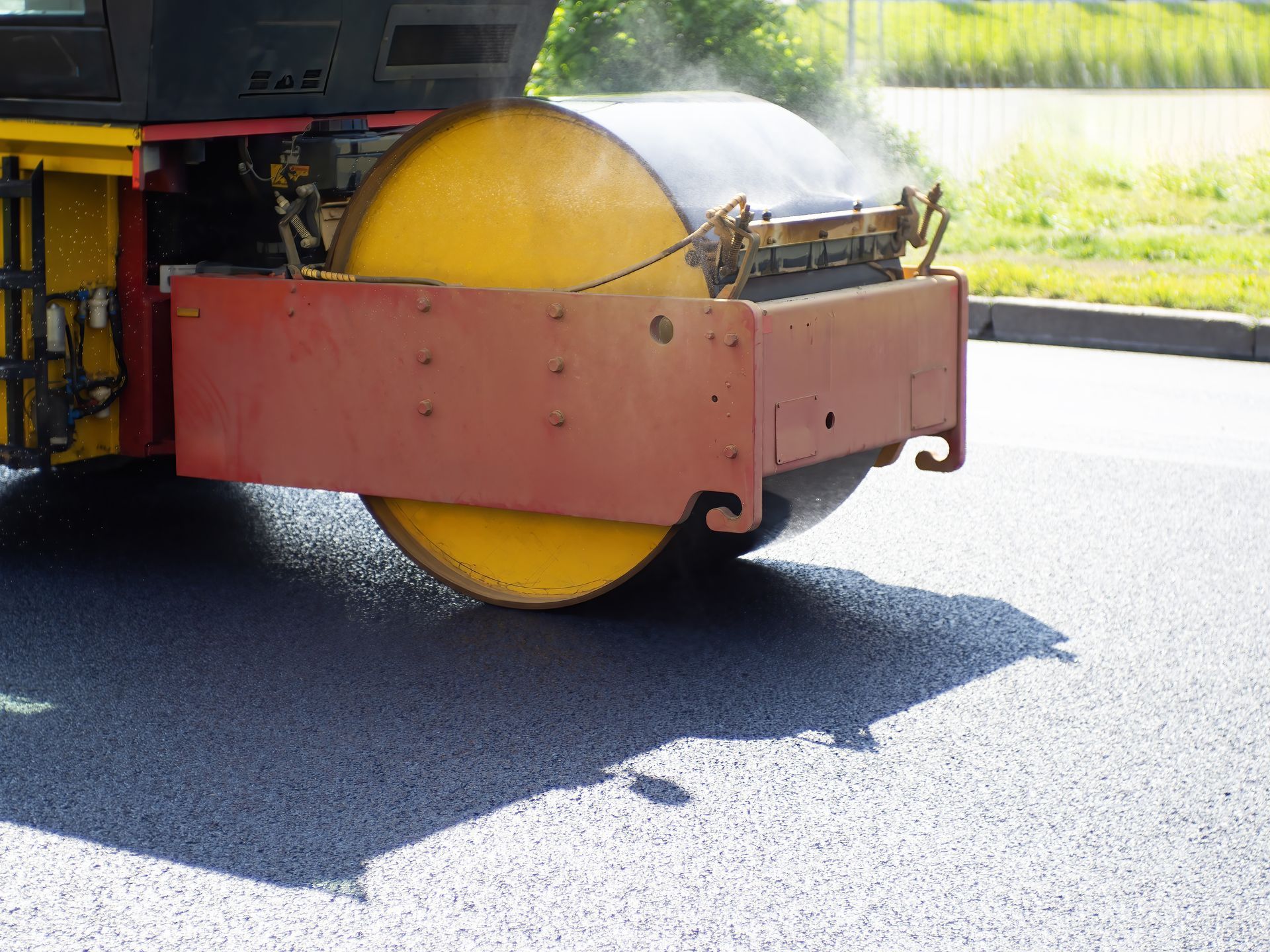 Road roller compacting fresh asphalt on a sunny day.