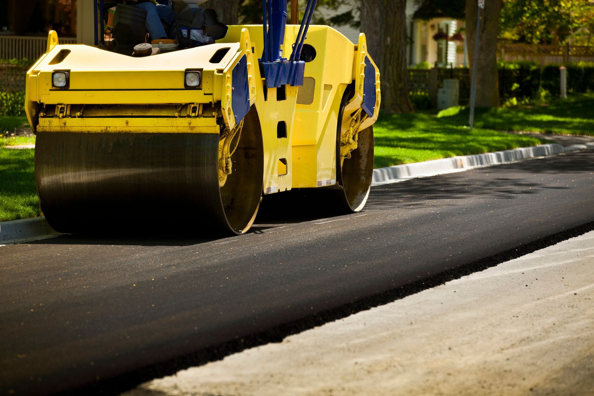 A yellow roller operated by a driveway paving contractor on a suburban street. A yellow roller operated by a driveway paving contractor on a suburban street.