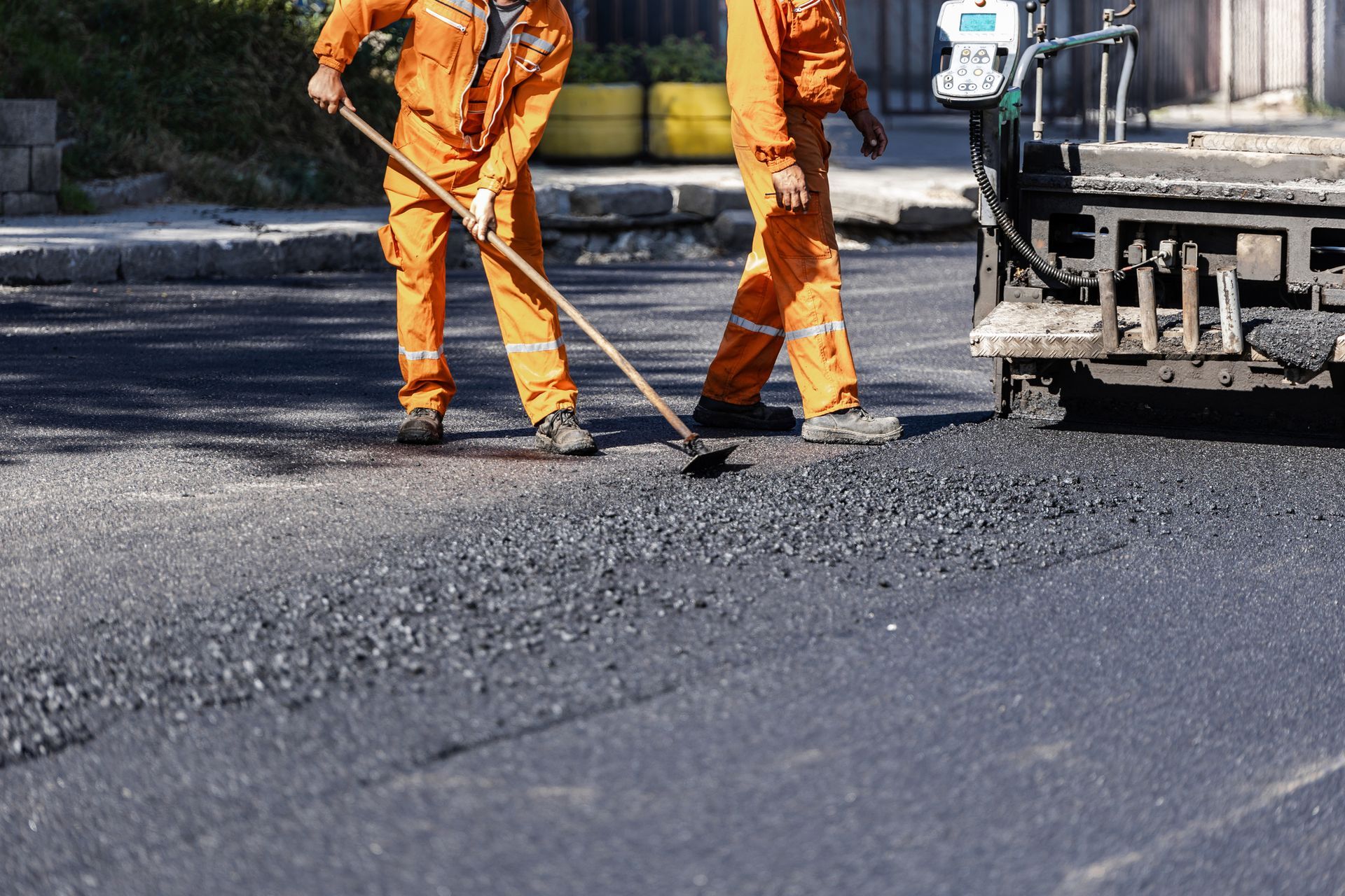 Two workers in orange coveralls paving a road with asphalt. Two workers in orange coveralls paving a road with asphalt.
