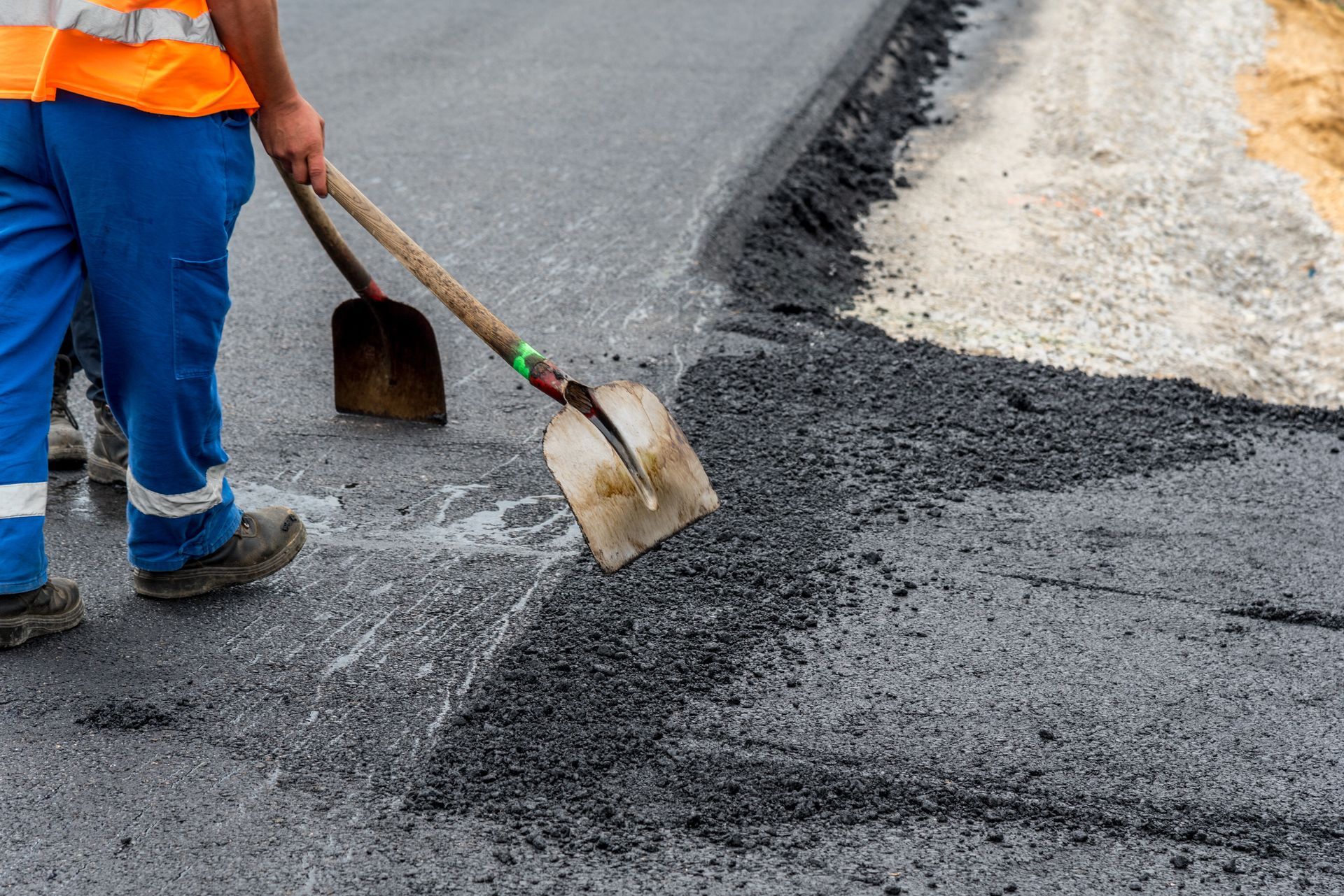 Close-up of construction site worker as he levels paving on road with a shovel.