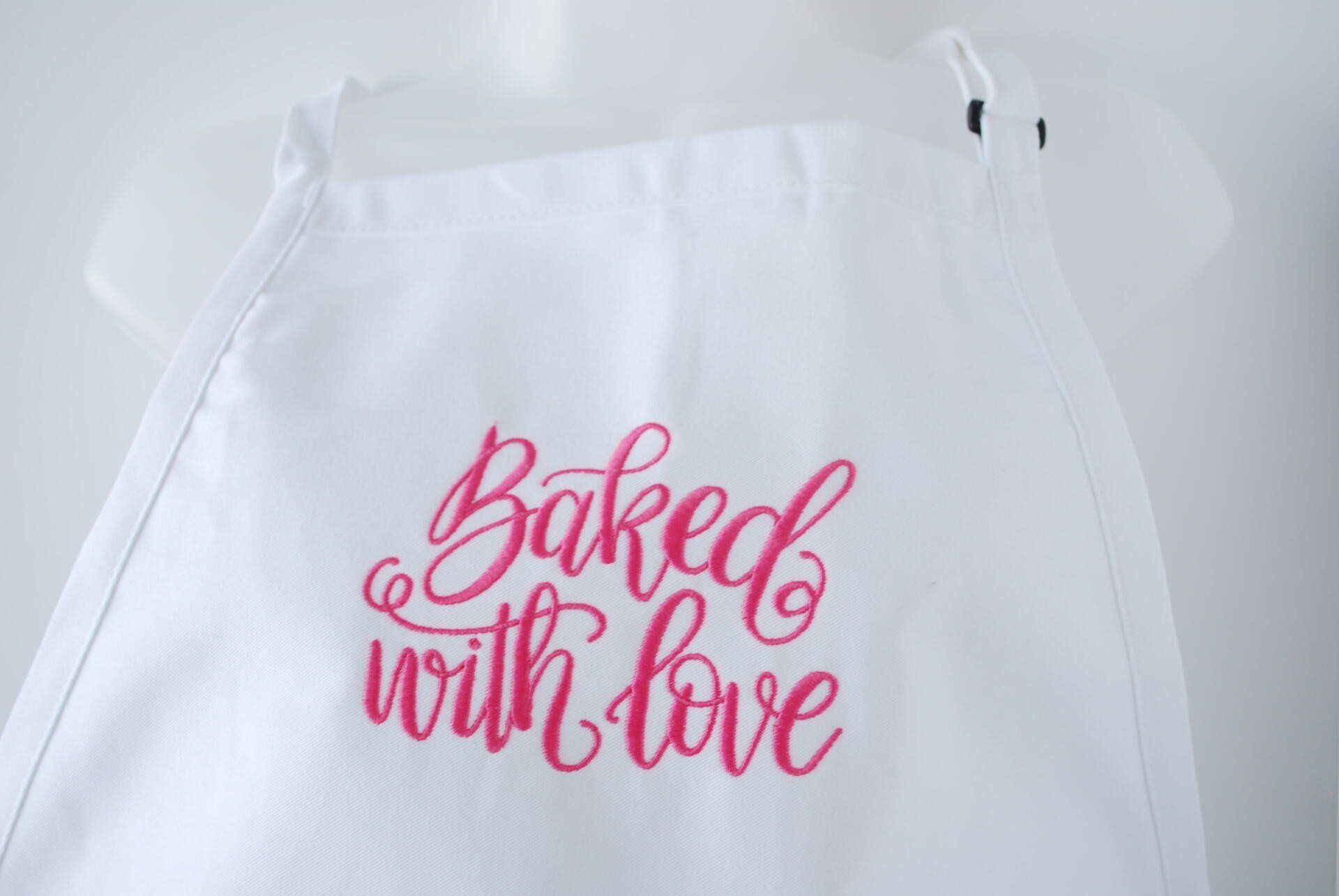 A white apron with the words Baked with Love embroidered on it