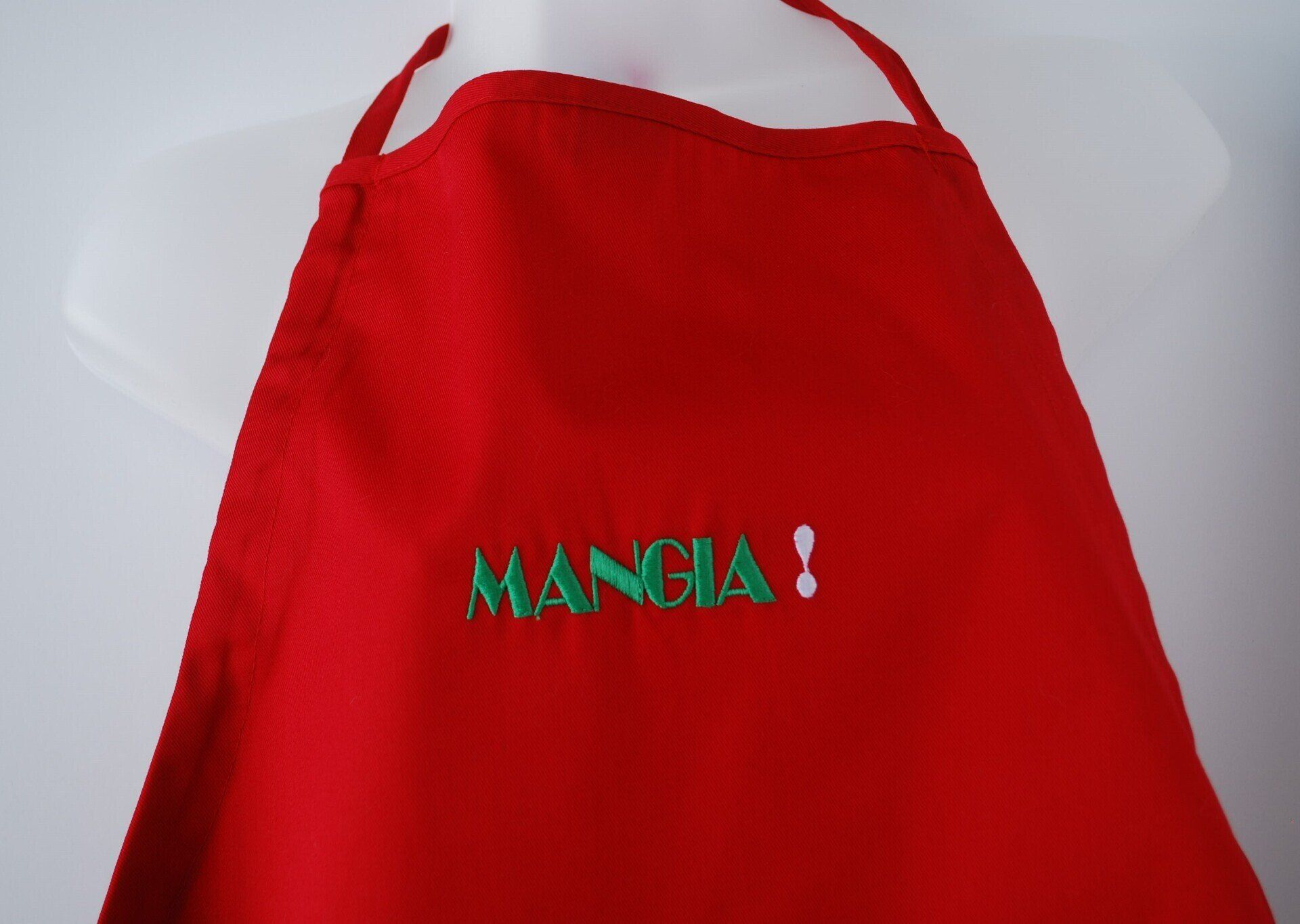 A red apron with the word Mangia embroidered on it