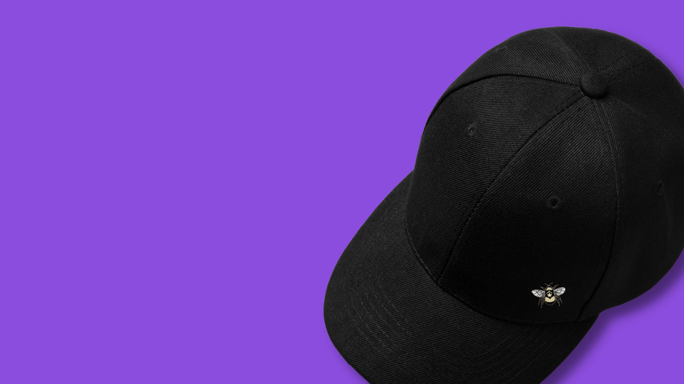 A black baseball cap with embroidered bee logo on a purple background