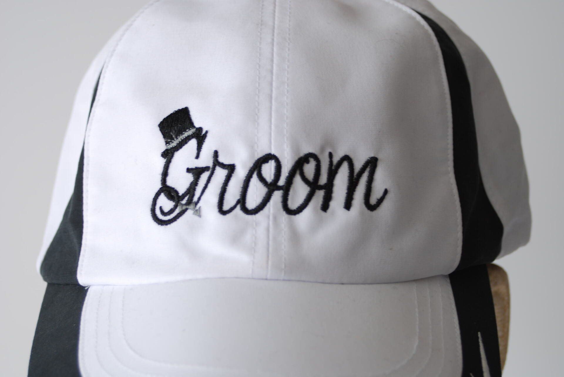 A white baseball cap with the word Groom embroidered on it in black