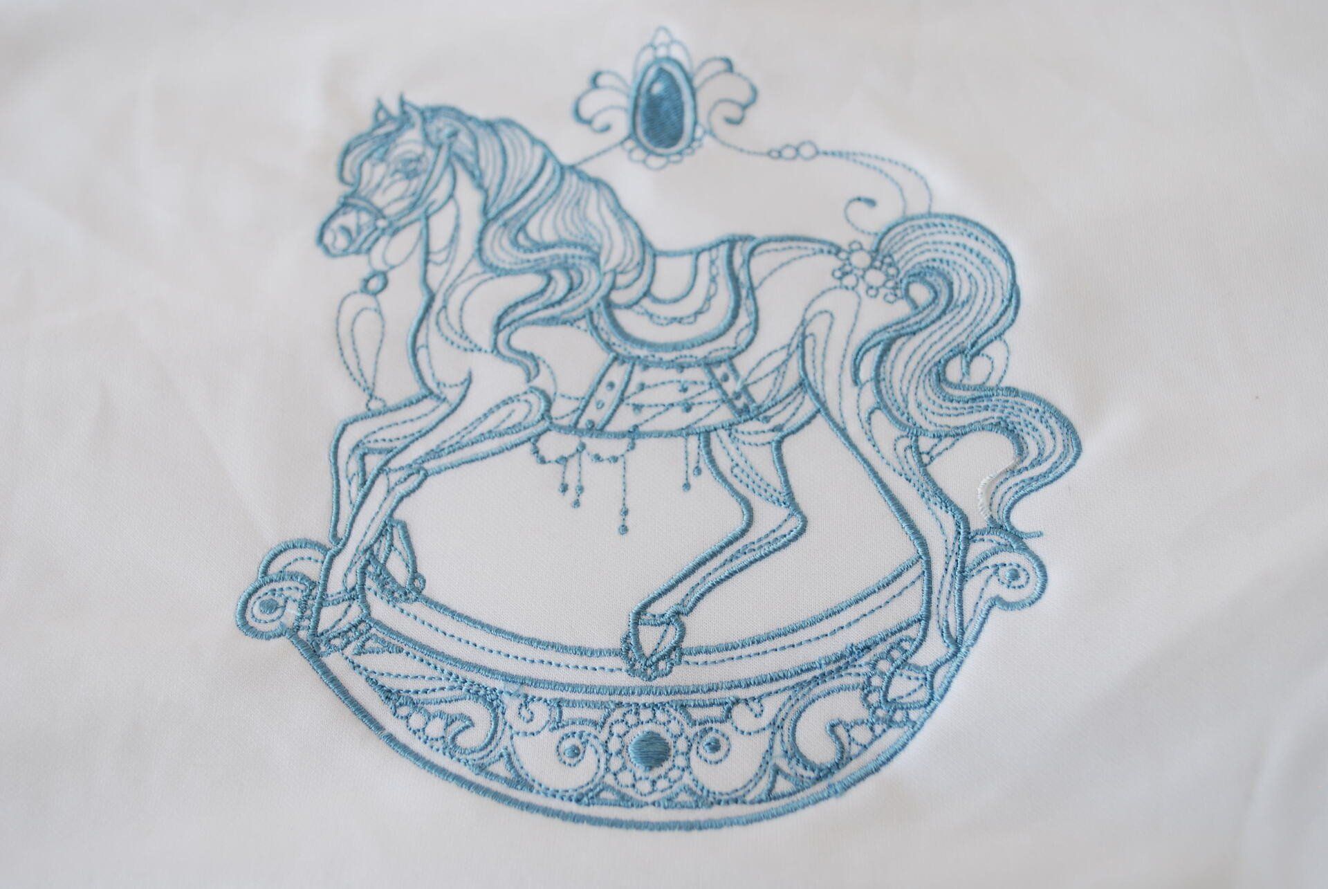 A light blue rocking horse embroidered on white cloth