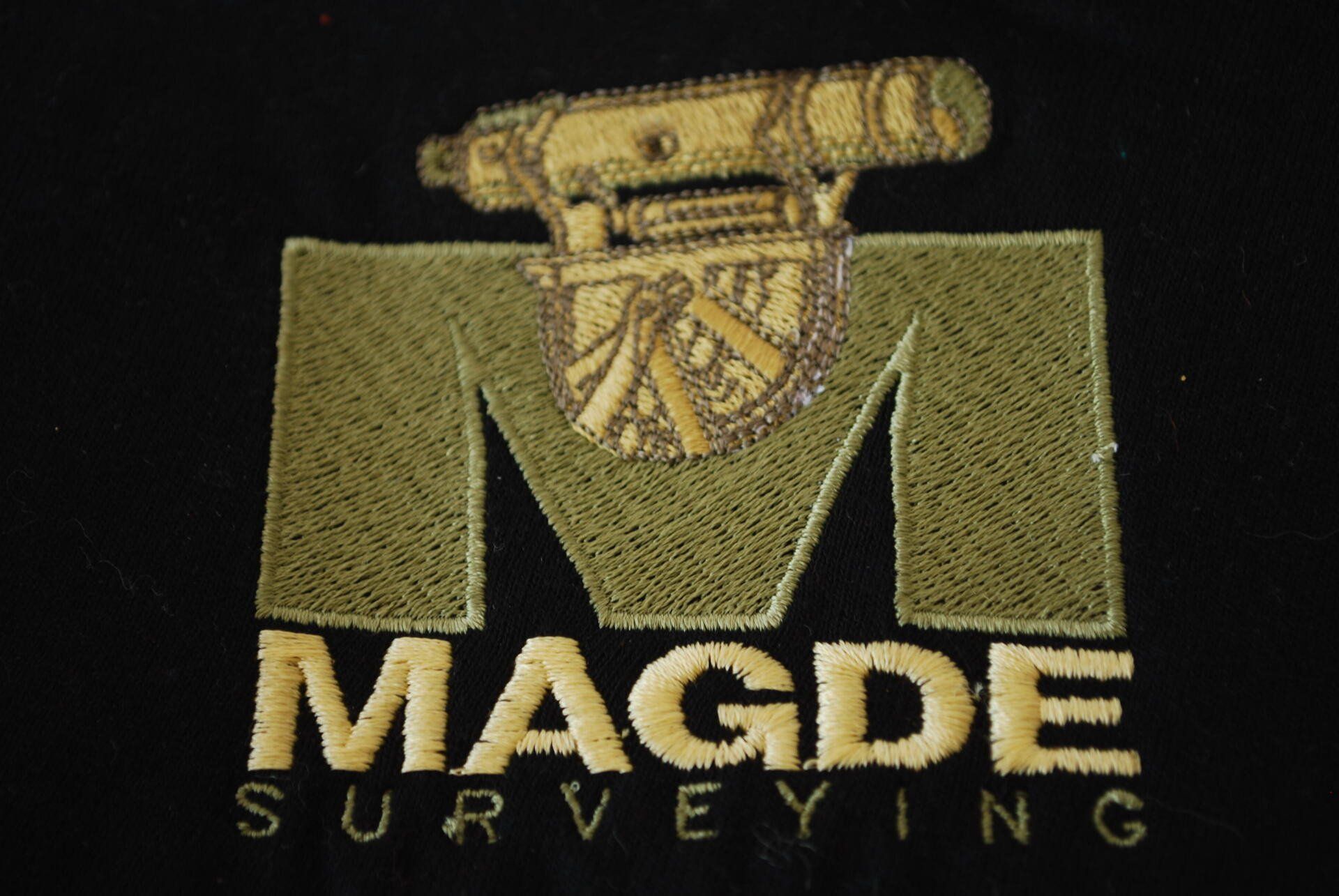 A logo for Magde Surveying embroidered on black apparel