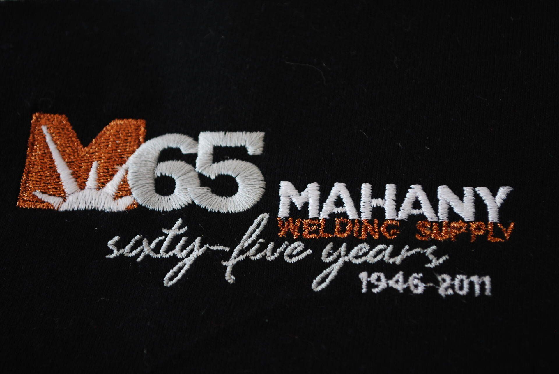 An embroidered logo for M65 Mahany Welding supply on black apparel