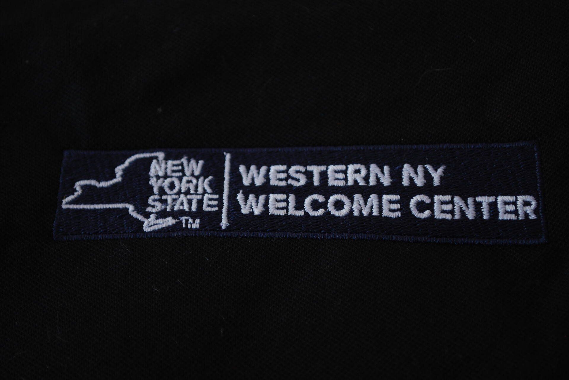 The New York State Welcome Center logo embroidered on black apparel