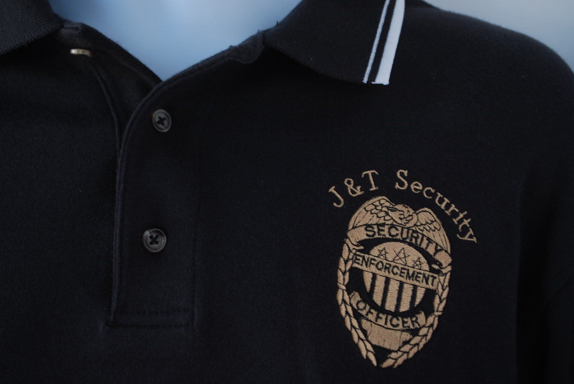 A black polo shirt with the J&T Security logo on it