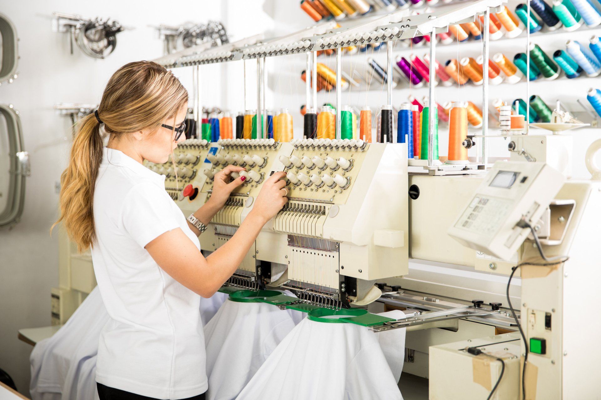 A woman in a white shirt is working on an embroidery machine