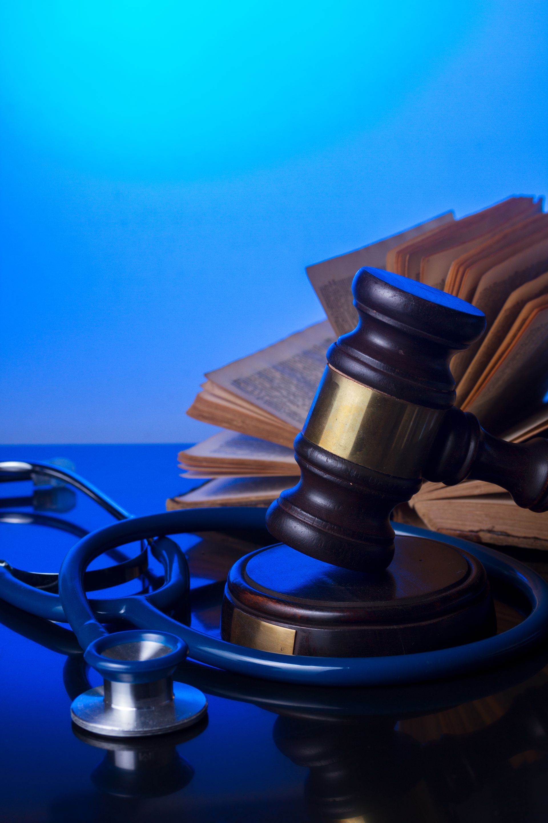 Gavel on a stand, stethoscope, and open books, on a reflective surface, blue background.